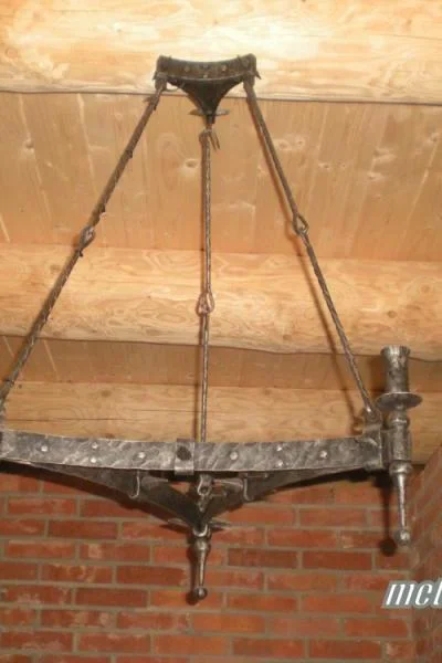 Trójkątna lampa wisząca na trzech zawiesiach. Misterne, ćwiekowane wykończenie z uchwytami na pochodnie do wnętrz średniowiecznych, karczm i pubów oraz do domów z bala.