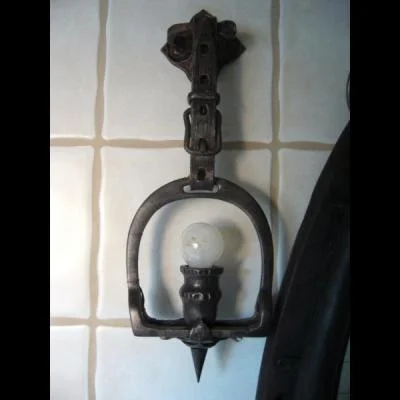 jednopunktowa lampa ścienna w formie strzemiona jeździeckiego wiszącego na stalowym pasie. Oryginalna metaloplastyka do wnętrz w stylu jeździeckim , retro i chalet