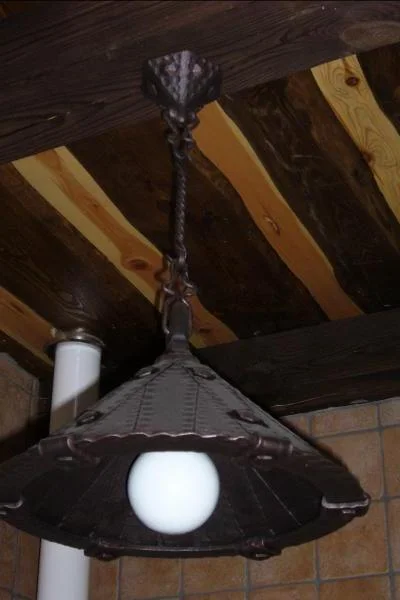 Masywna metalowa lampa sufitowa z nitowanym kloszem, rustykalne oświetlenie kierunkowe nad stół jadalniany.