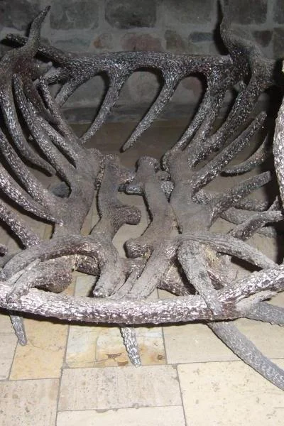 Artystyczny stojak kominkowy o rzeźbiarskiej strukturze przeplatających się metalowych poroży, unikatowe rękodzieło o głębokiej fakturze i surowym wykończeniu.